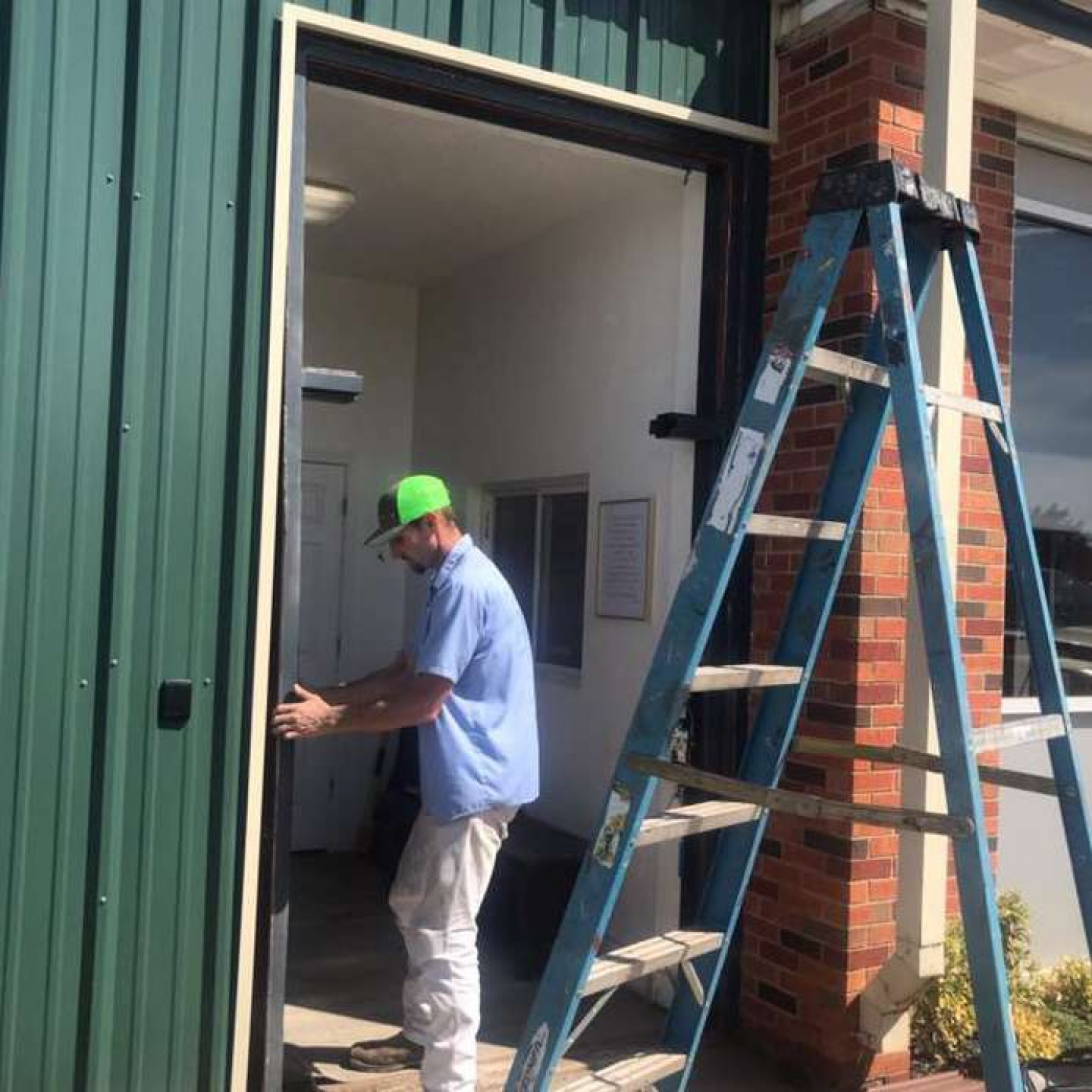 A door technician installing a door frame on a green metal building