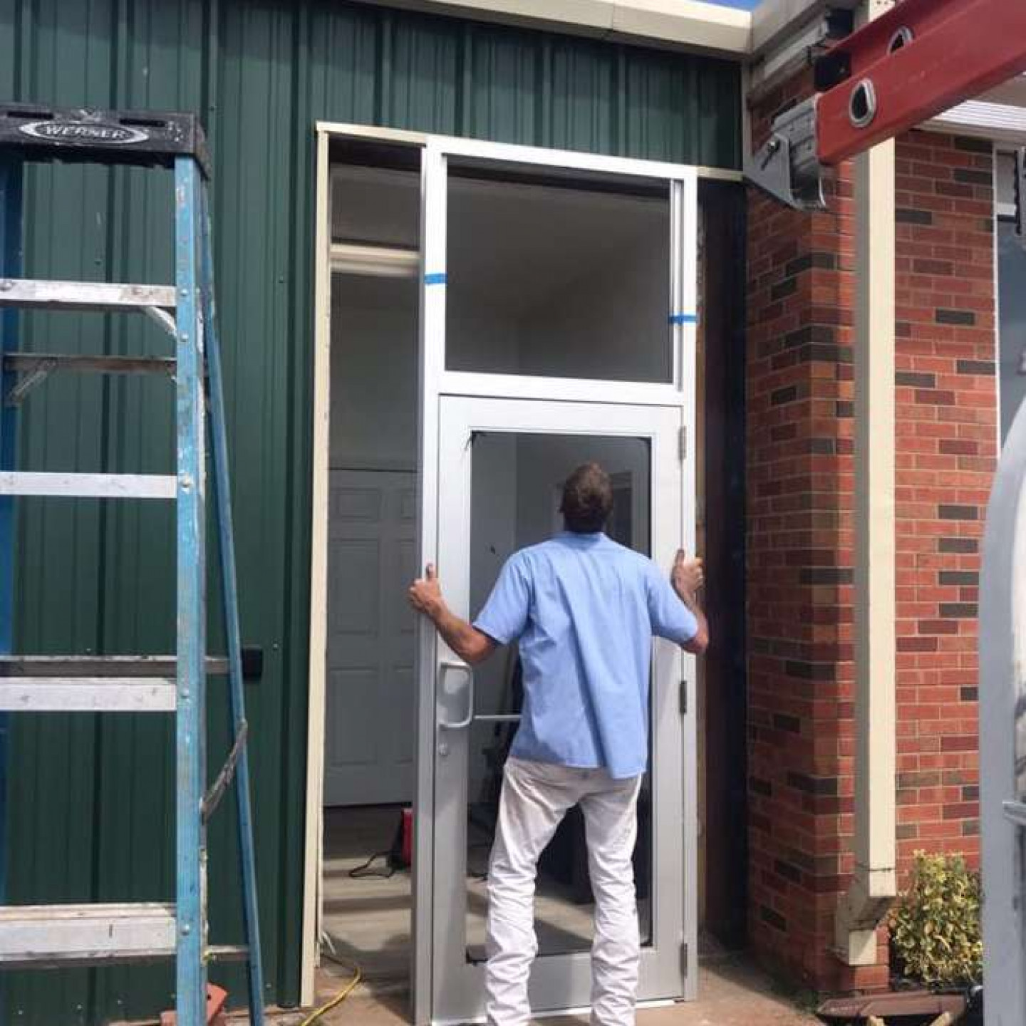 A door technician installing an aluminum glass entry door on a green metal building